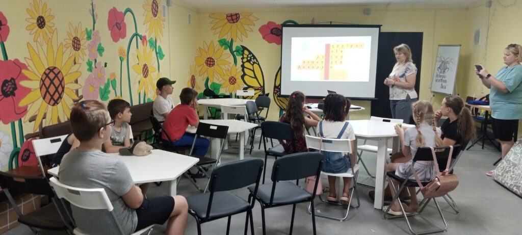Діти-учасники заходу "Міста-герої України" розгадують кросворд з назвами міст, який бібліотекарка проєктує на екран.
