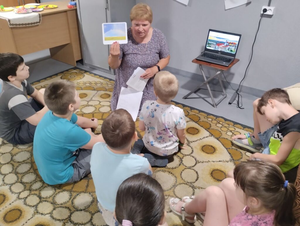 Учасники заходу спілкуються з бібліотекаркою, сидячи довкола на м'якому килимі