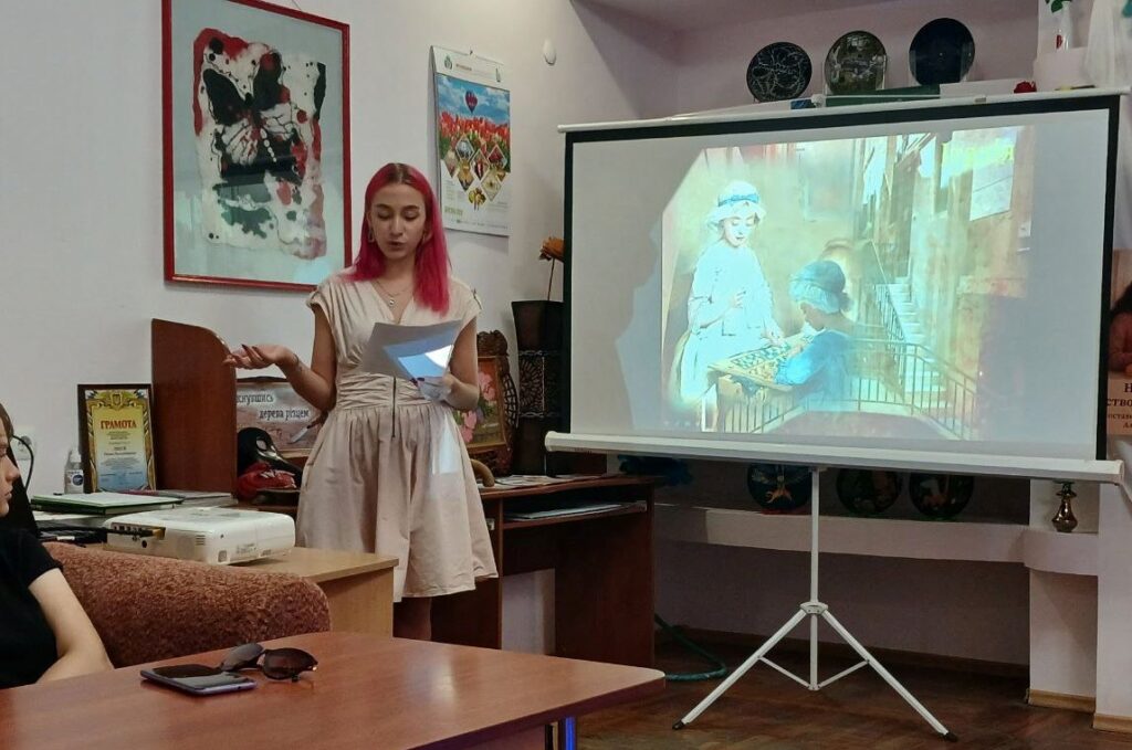 Бібліотекар розповідає про зображення гри в лото у живописі, демонструючи репродукції картин на великому екрані