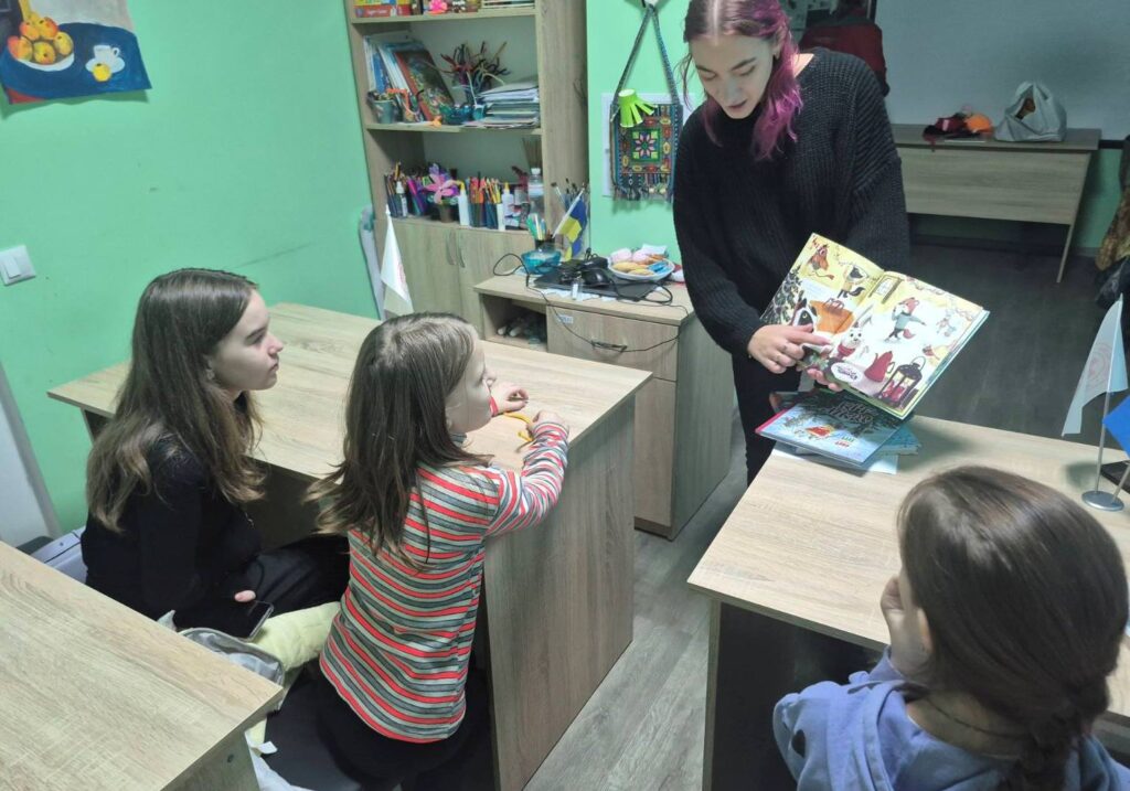 Діти розглядають ілюстрації в книзі, які показує бібліотекарка