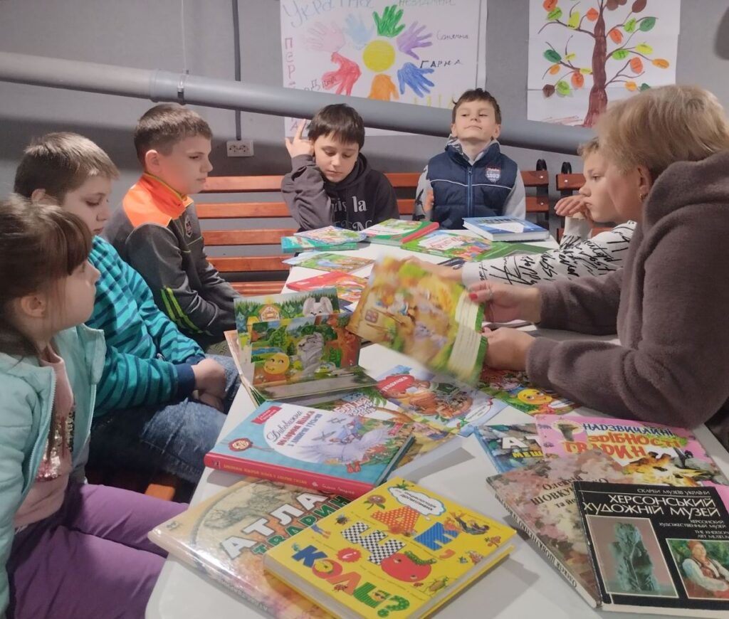 Учасники гри сидять довколо стоду і разом з бібліотекаркою знайомляться з книжками