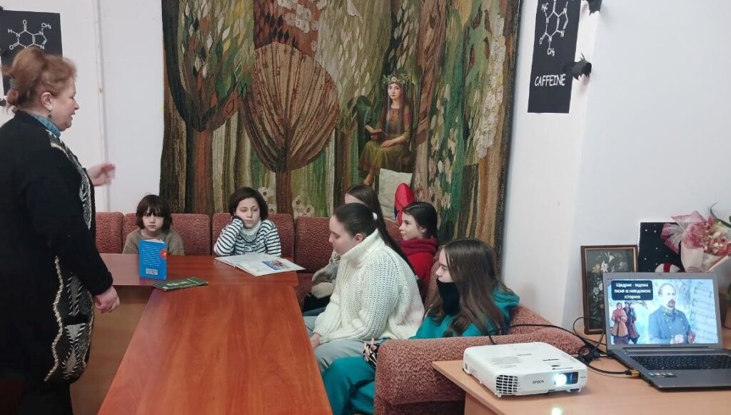 Бібліотекарка представляє дітям книги, в яких можна прочитати про "Щедрик" та про Миколу Леонтовича