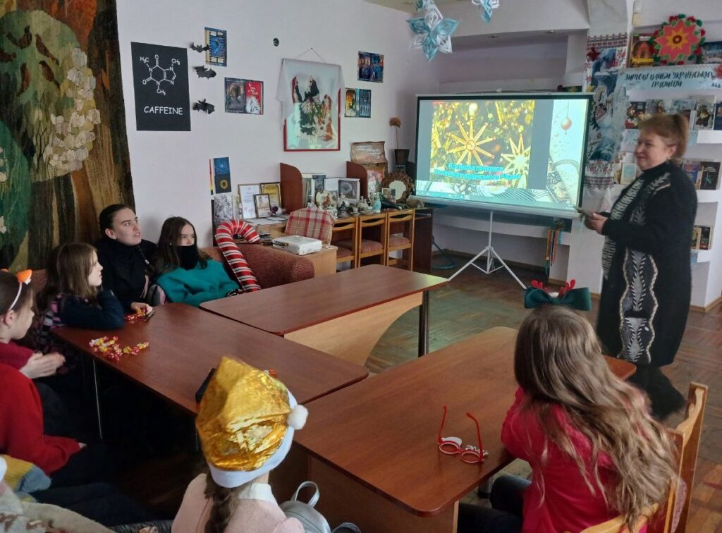 Діти слухають розповідь бібліотекарки, яка демонструє презентацію на великому екрані