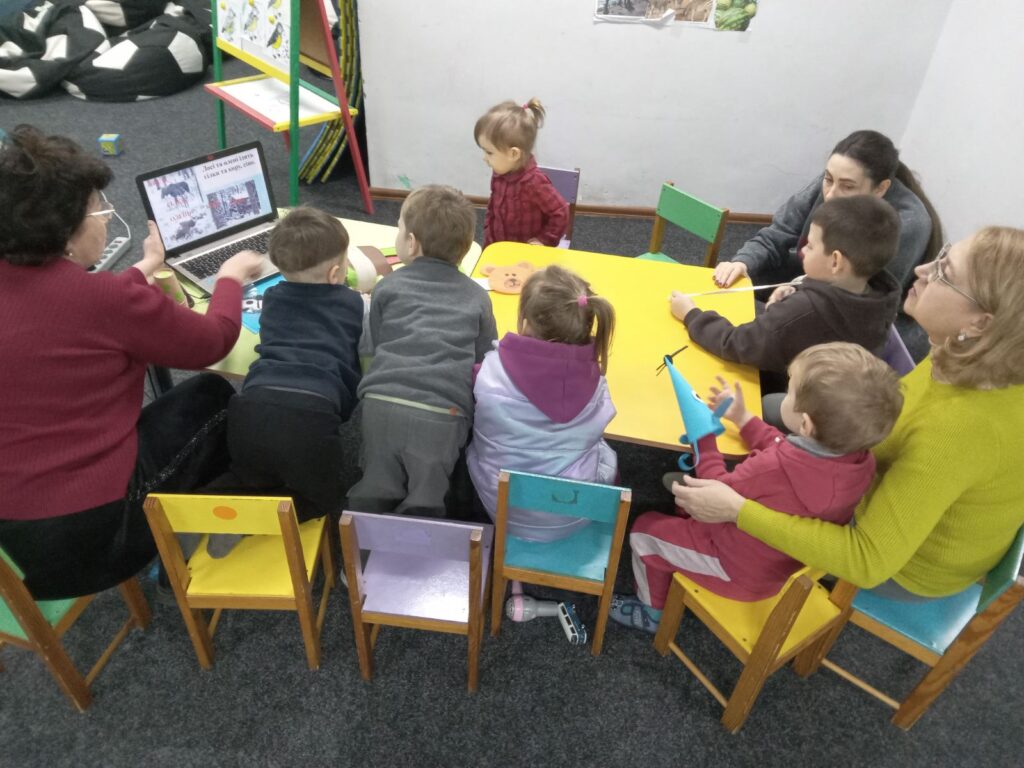Маленькі учасники програми слухають розповідь бібліотекарки про зимовий ліс та його мешканців