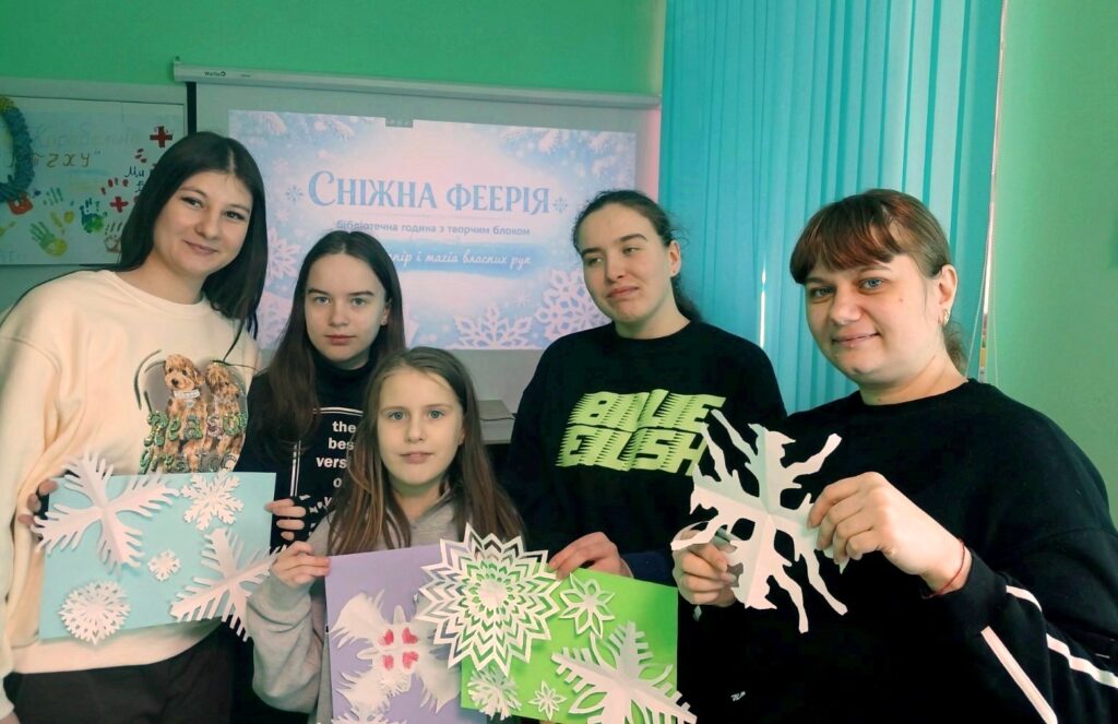 Учасники майстерки на фоні презентації на екрані та із сніжинками-витинанками в руках