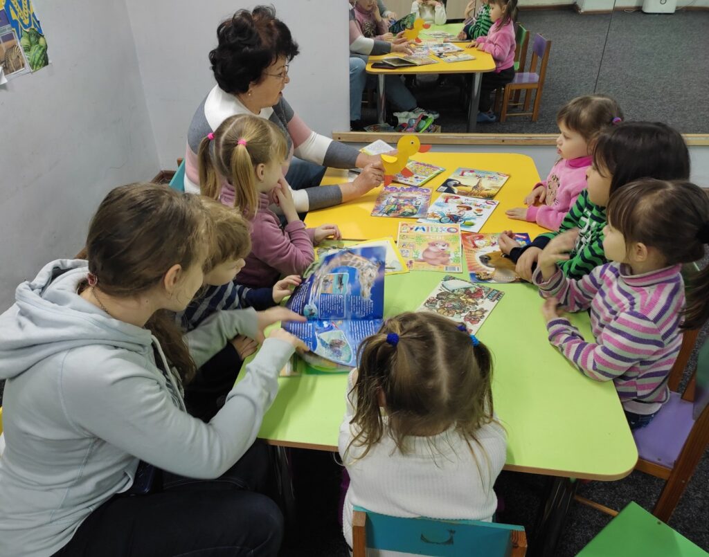 Учасники студії "Бібліомалята" слухають бібліотекарку, розглядаючи дитячі журнали