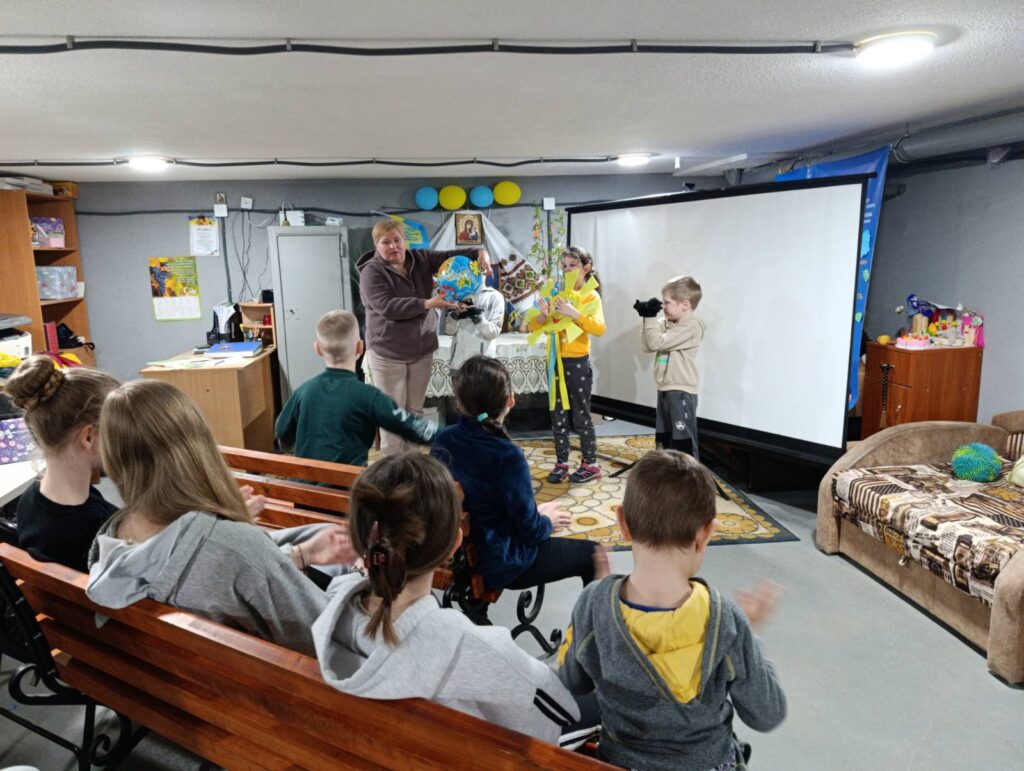 Бібліотекарка і діти моделюють рух Землі довкола Сонця, використовуючи глобус та малюнок-"Сонце" 