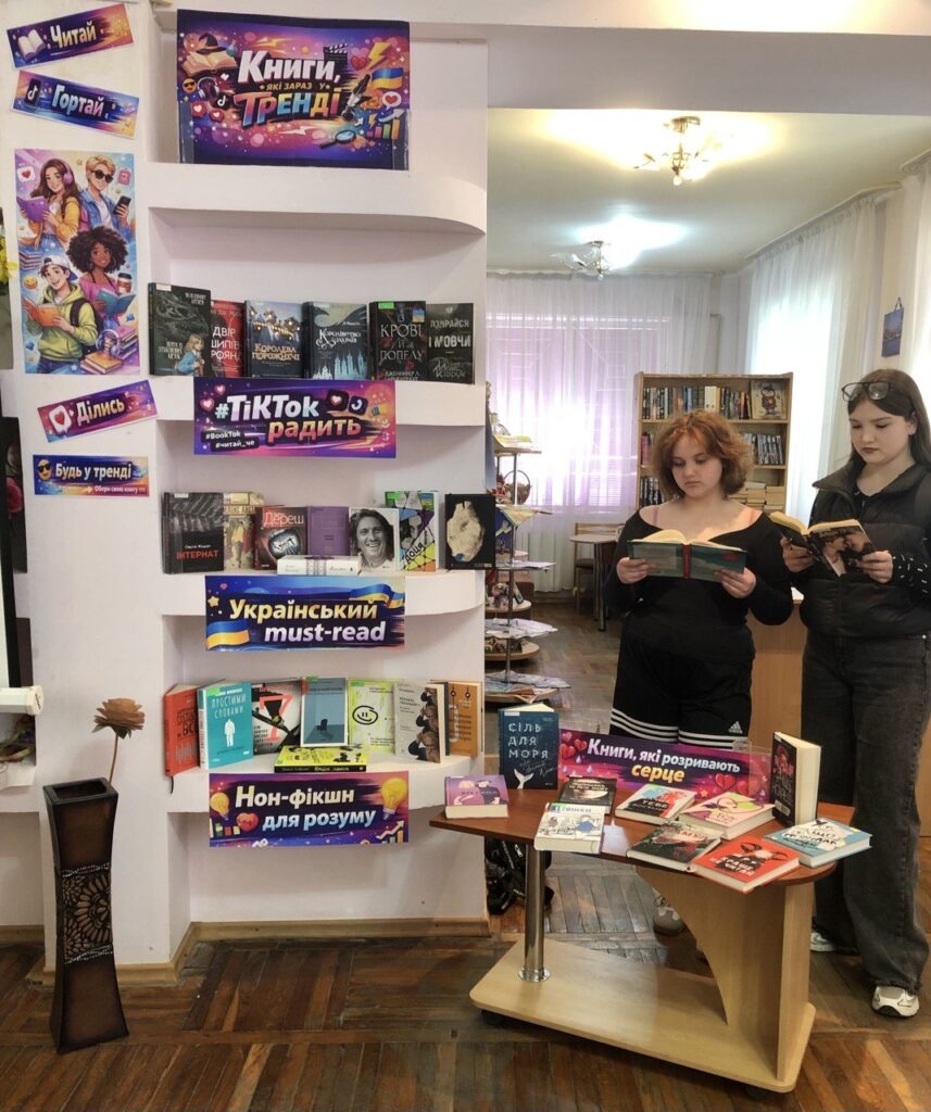 Двоє дівчат переглядають книжки біля експозиції виставки, - фото