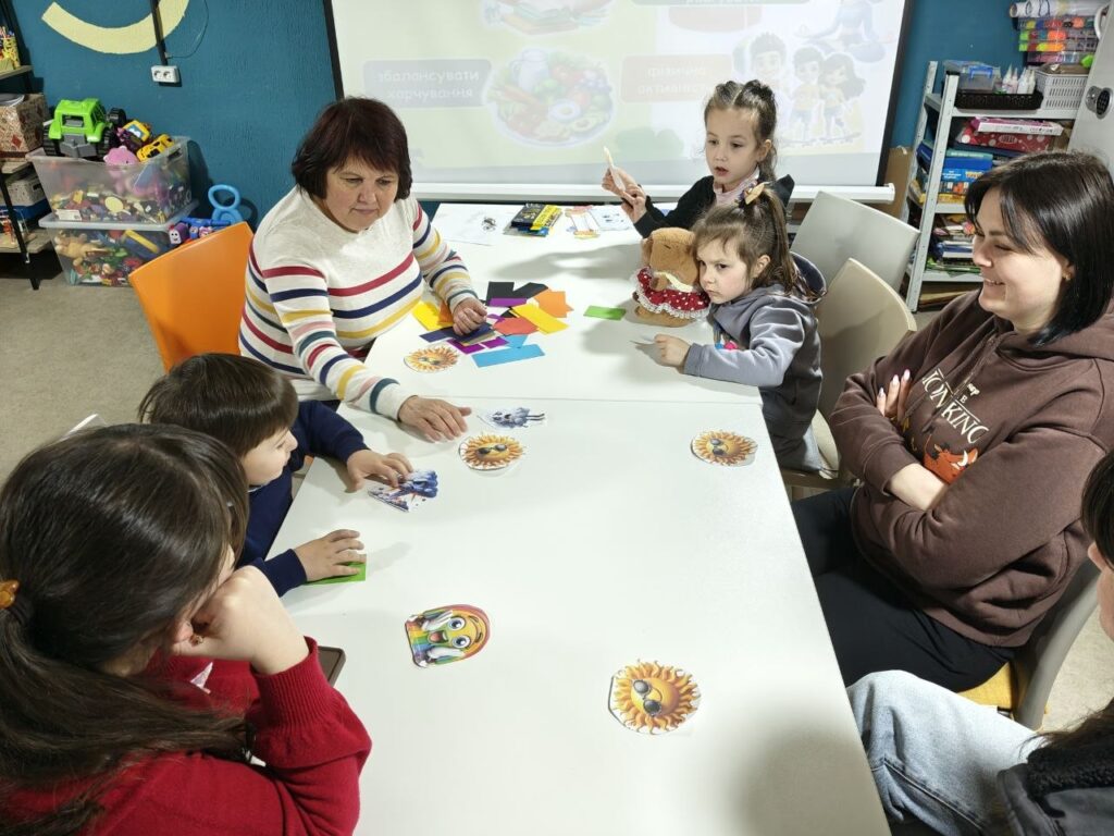 Учасники програми сидять разом за столом та розглядають малюнки, що символізують емоції