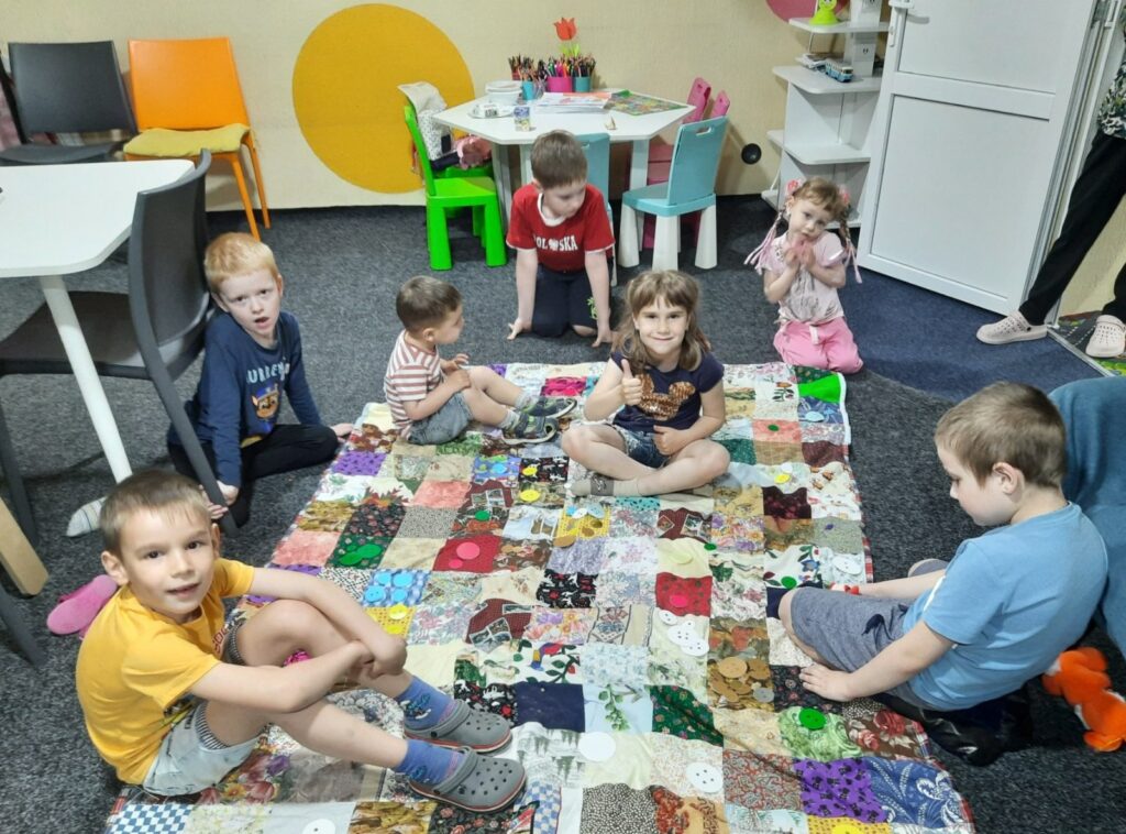 Діти сидять на клаптиковій ковдрі, розстеленій на килимі