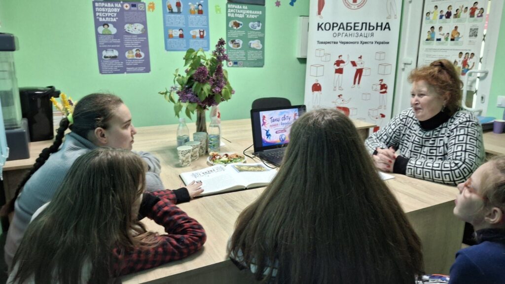 Учасники заходу слухають розповідь бібліотекарки про Міжнародний день танцю, переглядаючи презентацію на екрані ноутбука